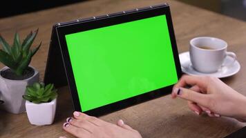 A woman is using a tablet with a cup of coffee and a green screen, ideal for digital content creation, app design, and product mockup presentations. video