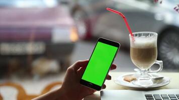 A woman using a smartphone with a green screen in a cafe ideal for showcasing mobile apps digital content creation and product mockup designs video