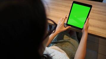 A woman using a tablet with a green screen in her home, ideal for app design, digital content creation, and mockup presentations in a comfortable environment. video