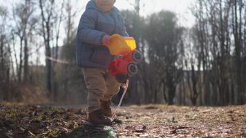 Happy baby child outdoor. Little toddler boy with toy car having fun on walk in park. Baby son smiling playing outdoor. Little child resting walking in nature. Little toddler child having fun on walk video
