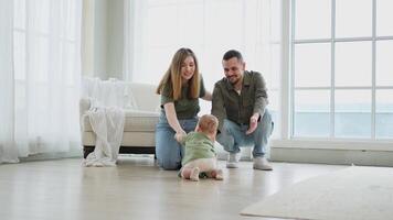 Baby development. Little infant girl making first steps at home. Happy mother father looking at toddler child walking in living room. Happy family at home. Mom dad supporting baby first steps video