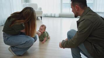 Baby development. Little infant girl making first steps at home. Happy mother father looking at toddler child walking in living room. Happy family at home. Mom dad supporting baby first steps video
