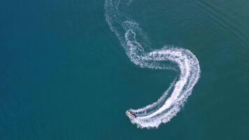 Aerial view of a motor boat forming a circle of waves and bubbles with its engines over the turquoise sea. Drone flight, summer vacation concept, banner. video