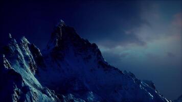Dramatic snow capped mountain peak illuminated by dusk in a clear sky video