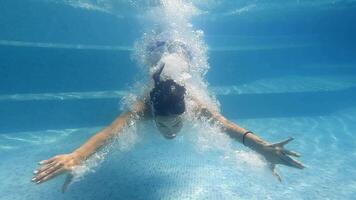 Detail view on young woman jumping in pool and splashing crystal clear water. Unrecognizable girl swimming under water in basin of hotel. Lady relaxing during summer vacation. Slow motion video