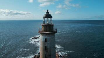 Top view of abandoned lighthouse in sea on sunny day. Clip. Abandoned lighthouse on rocks with waves of blue sea. Beautiful lighthouse on background of sea waves crashing on rocks video