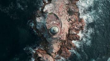 Top view of beautiful reef with waves and lighthouse. Clip. Single lighthouse on rocky ledge in blue sea on sunny day. Cinematic landscape of abandoned lighthouse on rocks in fantastic sea video