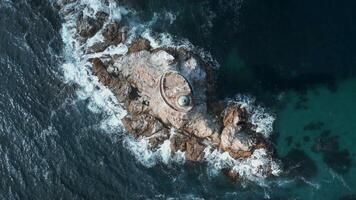 Top view of beautiful rocky cape with lighthouse. Clip. Cinematic landscape with blue waves and lighthouse on rock. Rocky cape with lighthouse in sea with waves on sunny day video