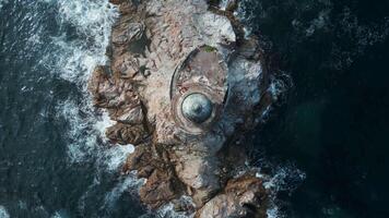 Top view of beautiful rocky cape with lighthouse. Clip. Cinematic landscape with blue waves and lighthouse on rock. Rocky cape with lighthouse in sea with waves on sunny day video