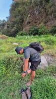 A male adventurer is trying to cross a small river which is very clear and beautiful because it is surrounded by green grass. Footage of a man crossing a river with a beautiful view video