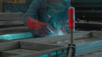 Man in mask works with welding metal structures at factory. Creative. Welder in equipment works at industrial plant. Worker with welding and welding sparks from metal video