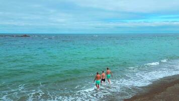 Top view of people running into sea. Clip. Men run to swim in blue sea on background of cloudy horizon. Men run to swim on coast of beautiful sea with reefs video