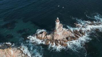 Top view of dramatic landscape of rocky island and lighthouse in sea. Clip. Cinematic fairy-tale landscape of rocky cape and lighthouse in ocean. Magical landscape of rocks and abandoned lighthouse in video