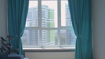 Cozy room with white walls and blue curtains. Media. Big window with a building behind it. video