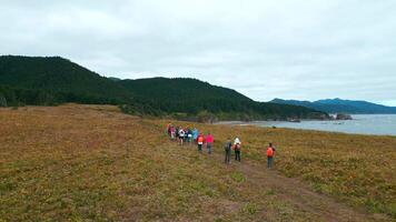 Top view of tourists walking along mountain coast trail. Clip. Hikers walk along mountain coast road on cloudy day. Tourists walk along northern mountain coast on background of sea and forests video
