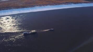 Floating barge on background of spring landscape. Clip. Top view of floating barge on river on background of snowy shore. Sunny landscape with floating barge on river video