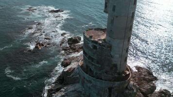 Top view of abandoned lighthouse with sea waves. Clip. Amazing landscape of abandoned lighthouse in ocean on sunny day. Seascape with abandoned lighthouse on rocks and beautiful blue waves video