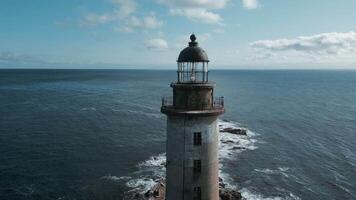 Top view of abandoned lighthouse with sea waves. Clip. Amazing landscape of abandoned lighthouse in ocean on sunny day. Seascape with abandoned lighthouse on rocks and beautiful blue waves video