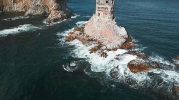Top view of abandoned lighthouse with sea waves. Clip. Amazing landscape of abandoned lighthouse in ocean on sunny day. Seascape with abandoned lighthouse on rocks and beautiful blue waves video