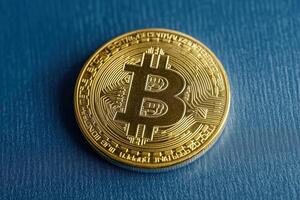 A golden Bitcoin coin resting on a blue surface. photo