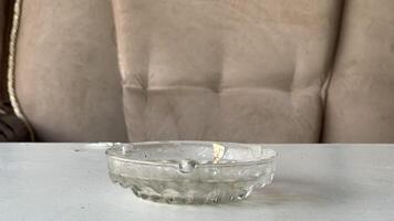 Clear glass ashtray placed on a table beside a soft couch photo