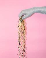 Hand holding shiny ribbon strands against a pink background in modern creative setting. photo