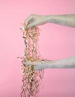 Hands adorned with glitter hold shiny streamers against a pink background. photo