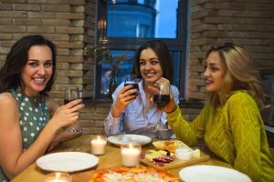 Three female friends toasting with red wine in the kitchen photo