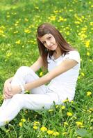 a girl sitting on a grassy field with dandelions photo