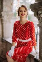 Smiling woman wearing red polka dot dress and white gloves posing on balcony photo