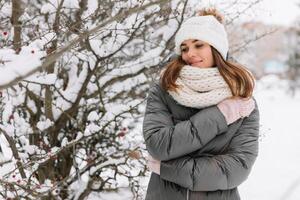 Young woman in winter attire embraces the snowy scenery, cuddling near a bush adorned with red berries photo
