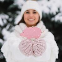 Girl in a white cap, sweater and mittens holding toy pig outside at winter snowy cold day, ready to celebrate new year and Christmas. photo