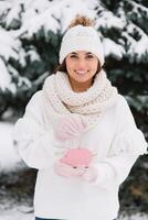Girl in a white cap, sweater and mittens holding toy pig outside at winter snowy cold day, ready to celebrate new year and Christmas. photo