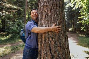 A young man with a backpack in the woods. An attractive tourist touches a large tree in the forest photo