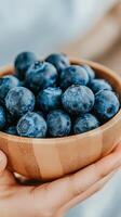 Freshly picked blueberries in a wooden bowl surrounded by green leaves photo