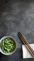 Fresh edamame in bowl with chopsticks on dark surface ready for a nutritious snack photo