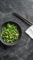 Fresh edamame in bowl with chopsticks on dark surface ready for a nutritious snack photo