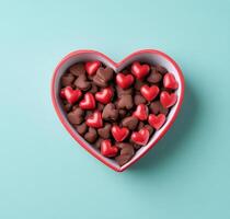 Heart shaped box filled with red and dark chocolates on a light blue background photo