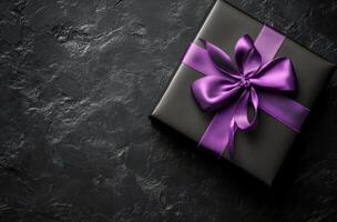 Elegant black gift box with purple ribbon placed on a textured dark surface for a special occasion photo