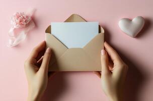 A person holding a blank envelope with a ribbon and heart decoration on a soft pink background photo