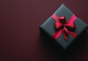 Elegant black gift box with a red ribbon against a deep red background photo