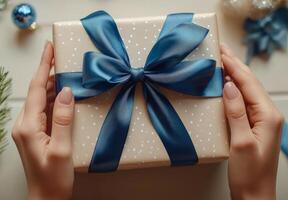 A person holds a beautifully wrapped gift with a blue ribbon and polka dots on a pink background photo