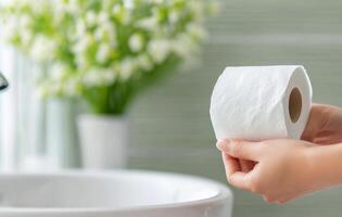 Hands holding a roll of toilet paper near a sink and flowers in a bright bathroom setting photo