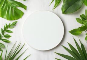Circular white plate surrounded by vibrant green leaves on a light wooden surface photo