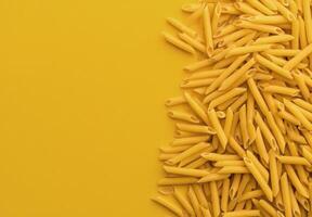 Dried yellow pasta pieces scattered on bright yellow background in a creative layout photo