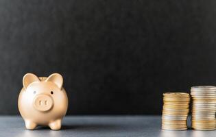 Golden piggy bank beside stacked coins on grey surface symbolizes saving money and investment photo