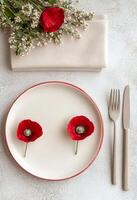 Red poppy flowers on a white plate with fork and napkin on a textured gray surface photo