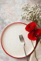 Red poppy flowers on a white plate with fork and napkin on a textured gray surface photo