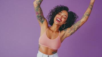 Joyful woman with curly hair and tattoos posing against a purple background during daytime photo
