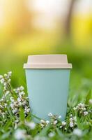 A pastel green coffee cup resting on grass surrounded by small white flowers in warm sunlight photo